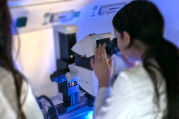 A girl in a lab coat looks through a microscope.